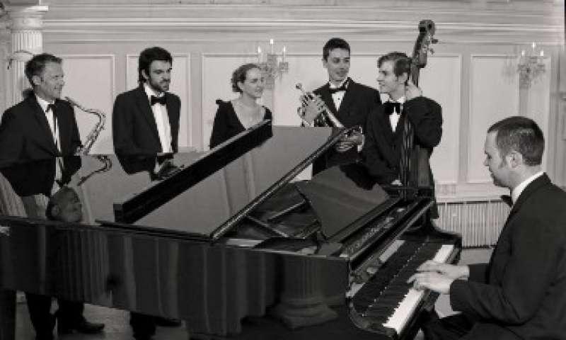 Matt Hodge Jazz Band gathered around a piano playing